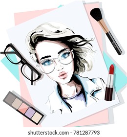 Stylish table set with hand drawn woman portrait, papers, lipstick, eyeglasses, brush and eyeshadows. Sketch. Vector illustration.