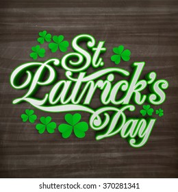 Stylish text St. Patrick's Day with beautiful shamrock leaves on wooden background.