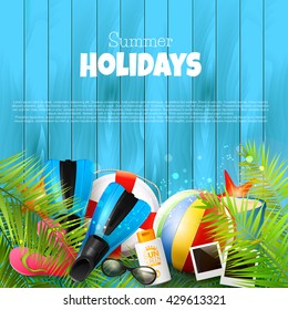 Summer background with beach ball, sunglasses, palm leaves, diving fins, flip-flops, safety circle and bucket on blue wooden background