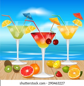 Summer cocktails with pieces of fruit on wooden table and with beach on background