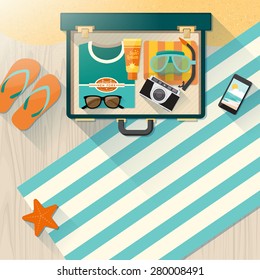 Summer holidays on the beach concept, open vintage suitcase with towel, scuba mask, camera, sunglasses and t-shirt on wooden flooring and sand