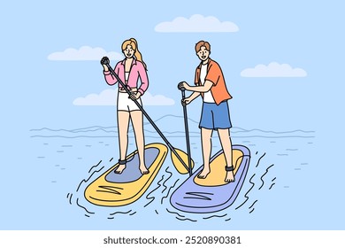 Surfing on SUP boards is practiced by man and woman using paddles to navigate river on summer weekend. Man and woman surfers stand on SUP boards, engage in active recreation at hot resort