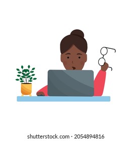 Surprised African American woman holding glasses in her hand while sitting with laptop. Woman working with a computer. Workflow concept, freelance worker. African American girl sitting at the table