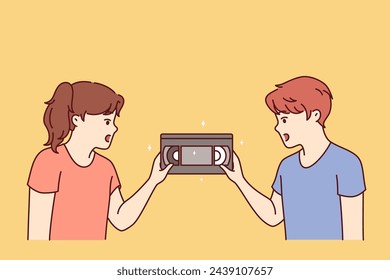 Surprised children are looking at film video cassette with movie recorded for VHS player from last century. Little kids see VHS tape for first time to play video on TV and dont know how to run cinema