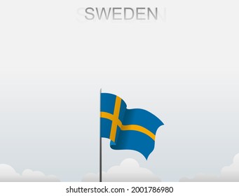 The Swedish flag flutters on a pole that stands tall under a white sky