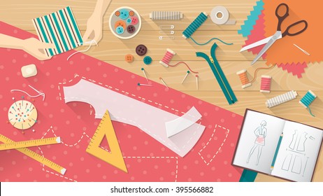 Tailor working and sewing a shirt, sewing equipment, patterns and sketchbook on the work table, dressmaking concept