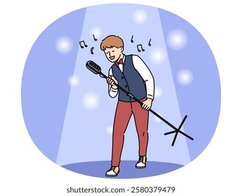 Talented boy singer holds professional microphone on tripod and performs at concert standing in light of spotlight. Happy teenage child singer dreams of becoming star and touring world