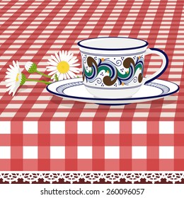 Tea cup on checkered tablecloth with daisies