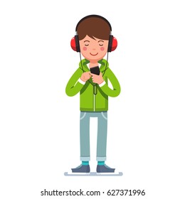 Teen boy in big headphones listening to music on mobile phone. Young man wearing hoodie, jeans and kids standing and tapping smartphone. Flat style character vector illustration isolated on white. 