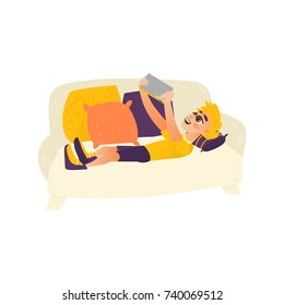 Teenage boy lying on sofa, using tablet, kids and technology, funny flat cartoon vector illustration isolated on white background. Flat cartoon portrait of teen boy playing with tablet, lying on sofa