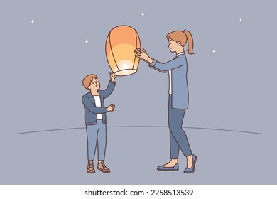 Teenage boy together with older sister, launch air fire lantern standing on street under starry sky. Mom helps son send air lantern in flight enjoy communication with child on summer evening 