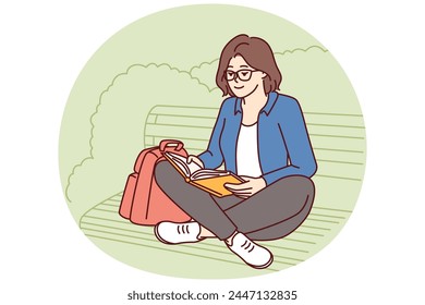 Teenage girl is reading book sitting on park bench enjoying good summer weather and intriguing plot of novel or fiction. Young woman spends leisure time outdoors doing self-education