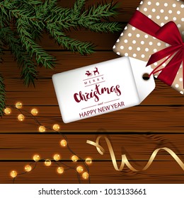 Template square holiday background. Wooden boards. Green branches and a garland, a gift with a red bow, a gold ribbon. Inscription Lettering "Happy New Year and Merry Christmas" on a white tag. Vector