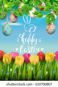 Template vector card with realistic colorful eggs, grass and tulips. Handwriting inscription Happy Easter and bunny. Bright sunny green background. Calligraphy. 3D. Decorated eggs hang on a tree.