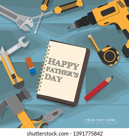 text Happy Fathers Day writing in notebook lay on blue mechanic wooden desk with yellow home repair tools