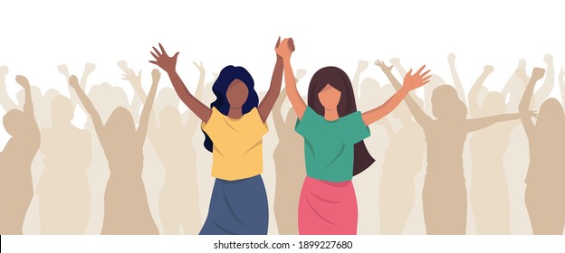 There is a crowd of people. They are happy. They rise the hands. There are two happy young girls in the foreground. One of them has dark skin, the other has light skin. They are holding hands. 