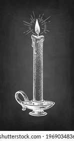 Thin candle burning in a candlestick. Chalk sketch on blackboard background. Hand drawn vector illustration. Retro style.