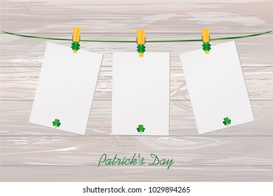 Three blank paper with green clovers hanging on a rope on a wooden clothespin. St.Patrick 's Day. Free space for your letters or advertising. Greeting card. Vector illustration on wooden background.