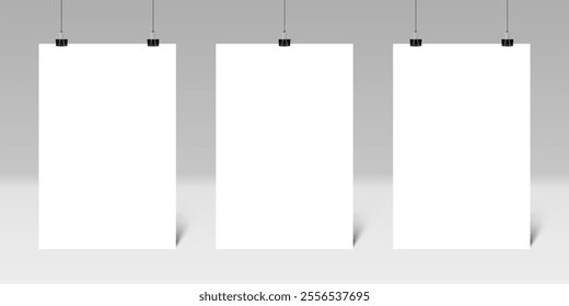 Three blank vertical posters hanging from binder clips on a gray wall create an ideal setting for displaying artwork or designs, enhancing any creative environment or presentation space