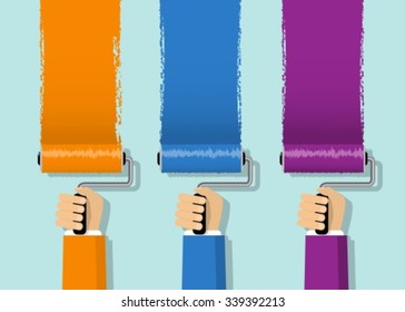 Three hands are holding rollers and paint the walls in different colors