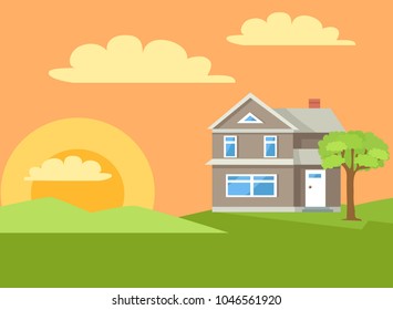 Three storey house of grey color with white front door and big window in rural countryside , situated on green grass lawn with bushes and trees at sunset