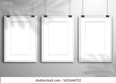 Three white blank paintings with passe-partout hanging on the binders near the wall. The shadow of the palm tree is on top. Mockup for gallery design