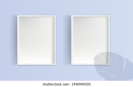 Three white blank picture frames hanging on the wall. The shadow of the leaves of the Monstera plant is on top. Mockup for design