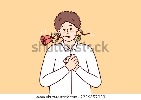 Timid young guy with rose in mouth clenching palms in front of chest looks at screen with head tilted to side. Man in white shirt hopes girl will like him and invite lover on date