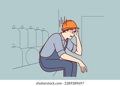 Tired man working in factory sits near production equipment holding head because of nervous job. Nervous factory worker in safety helmet needs psychological support due to poor working conditions