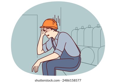 Tired man working in factory sits near production equipment holding head because of nervous job. Nervous factory worker in safety helmet needs psychological support due to poor working conditions