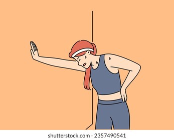 Tired woman runner with sweat on face, leaning against wall and trying to catch breath after long run. Young girl runner needs help of trainer due to excessive fatigue after workout.