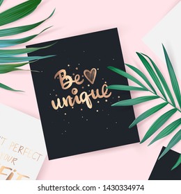 Top view with card. Be unique - Vector hand drawn lettering phrase. Motivation and inspiration gold quote. Flat lay with palm leaves