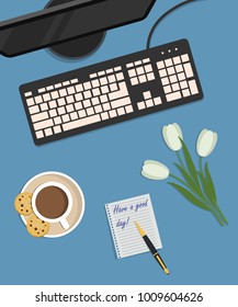 Top view of a desk background. There is a monitor and keyboard on a blue background. Also there is a cup of coffee with cookies and white tulips here. There is a note with the wish "Have a good day!"