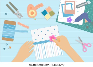 Top view of desk with scrapbook tools and elements: punch for eyelets,scotch tape.Hands of woman holding a flower.Vector illustration.