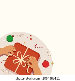 Top View Hand Holding Ribbon Of Gift Box With Baubles, Candy Cane And Copy Space On White Background.