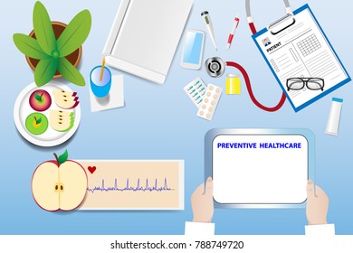 Top view of a medical table with doctor accessories. Hands are holding tablet with a sign Preventive healthcare. Cardiogram and the plate with apples are lying on the table. 