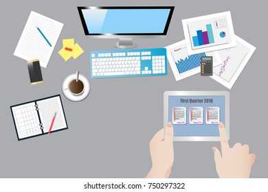 Top view of the office desk with office equipment. Hands are holding the tablet and the finger point to a  screen with calendar for the first quarter of 2018.