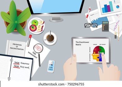 Top view of the office desk with objects, book of procrastination, open diary and ringing phone. Hands holding the tablet point to a screen with the Eisenhower Matrix.