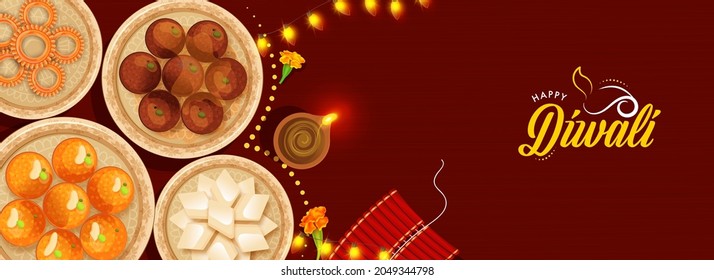 Top View Of Presenting Indian Sweets With Lit Oil Lamp (Diya), Firecracker Stripe And Lighting Garland On Red Background For Happy Diwali Celebration.