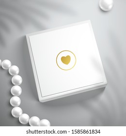 Top view of a white box with a golden heart and pearl beads. Realistic mockup for design with shadow of palm leaves