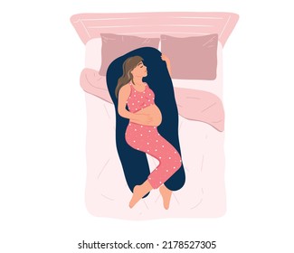 Top view young pregnant woman in pajamas sleeping on a maternity pillow on the bed. Comfortable sleeping position, healthy night sleep. Preparing for childbirth. Health and pregnancy care. Motherhood.