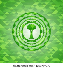 tree icon inside green emblem with triangle mosaic background