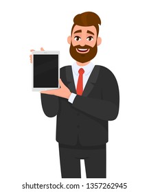 Trendy bearded business man showing/holding blank screen of digital tablet computer in hands. Millennial young man presents/introduces app, application from new digital pad. Modern technology concept.