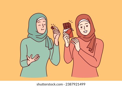 Two arab women eat chocolate and rejoice in rush of hormone of happiness, dressed in islamic scarves and clothes. Girls recommend trying chocolate made from natural cocoa beans and organic cream