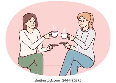 Two beauty girl friends drink hot coffee holding cups and saucers enjoy joint coffeebreak. Ladies dressed in casual style gossip during lunch break with hot non-drinks in hands