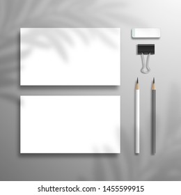 Two blank horizontal business cards, lead pencils, eraser and binder.  Flat lay mockup with palm tree shadow