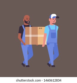 two couriers in uniform carrying cardboard box package mail express delivery service concept mix race workers holding parcel flat full length