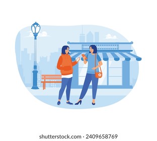 Two female friends walking together on a city street. They walked while looking at their cellphones and telling stories together. Urban panorama with pedestrians concept.