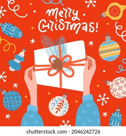 Two female Hands holding a gift box. Table surface with baubles and balls top view. Greeting card, banner or poster for Merry Christmas with lettering. Cute vector illustration in cartoon flat style.