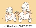 Two girls with hygienic mask on face rest lying on bed during rejuvenating spa treatment. Young mom and daughter in bathrobes use cosmetic masks to prevent wrinkles and get rid of acne